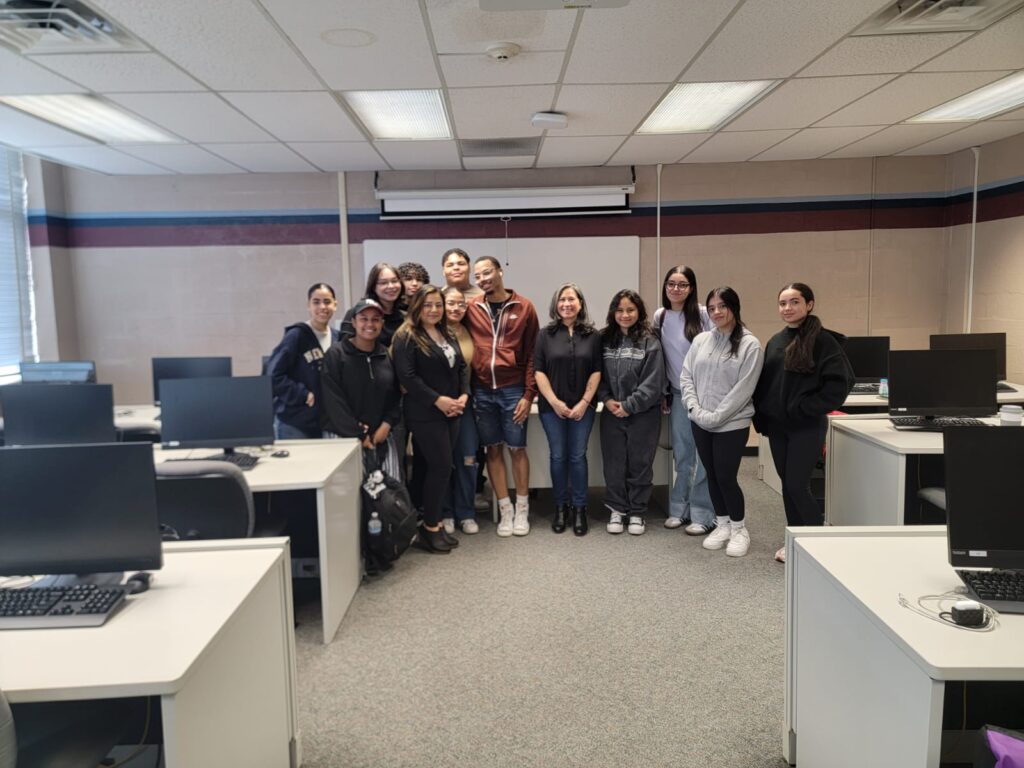 Carmen Molina Tamacas poses with Arianne Alvarez and a group of high school students inside a computer lab classroom.