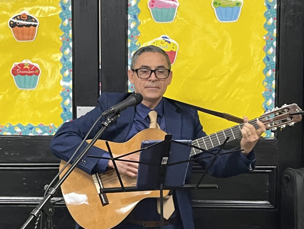 José Matías Guardado playing guitar and singing at a cultural event.