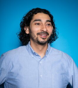 Luis Contreras, media scholar and Ph.D. student at Rutgers University, in front of a blue background