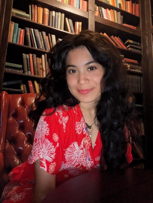 Allison Argueta-Claros seated in front of bookshelves, wearing a red patterned outfit and smiling.